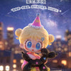 A cute figurine of a blonde character with pink hair and large blue eyes holding a black puppy, set against a blurred outdoor
