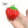 A bright red strawberry stress ball with a green leafy top is held in a person's hand.