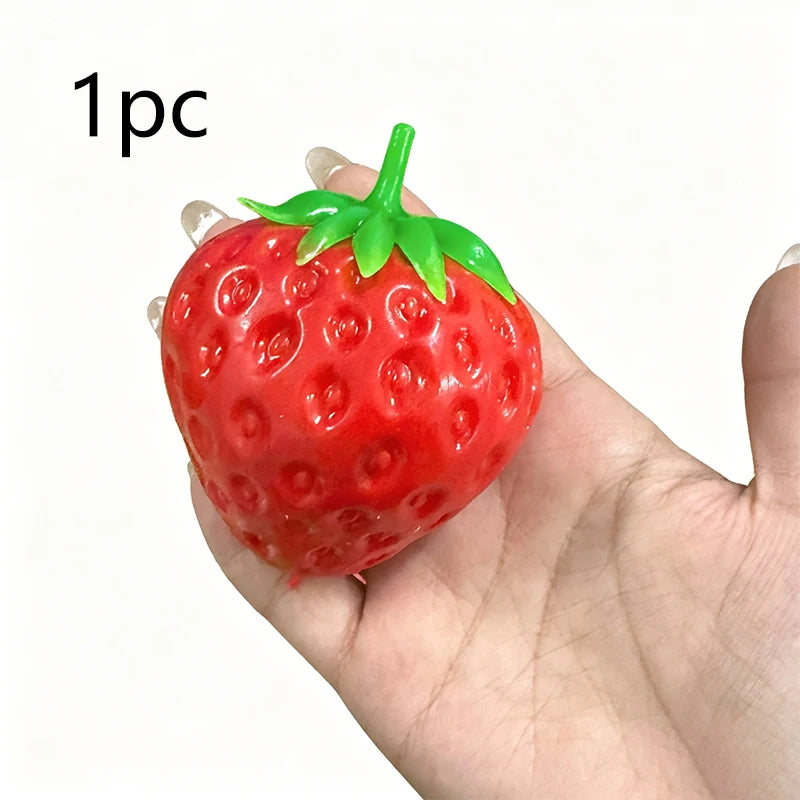 A bright red strawberry stress ball with a green leafy top is held in a person's hand.