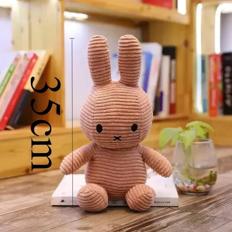 A soft, light brown Miffy plush toy resembling a rabbit is displayed on a wooden surface.