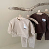 A beige baby long sleeve cartoon top and pants set hanging on a wooden rack.