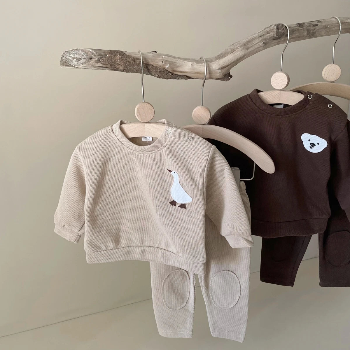 A beige baby long sleeve cartoon top and pants set hanging on a wooden rack.