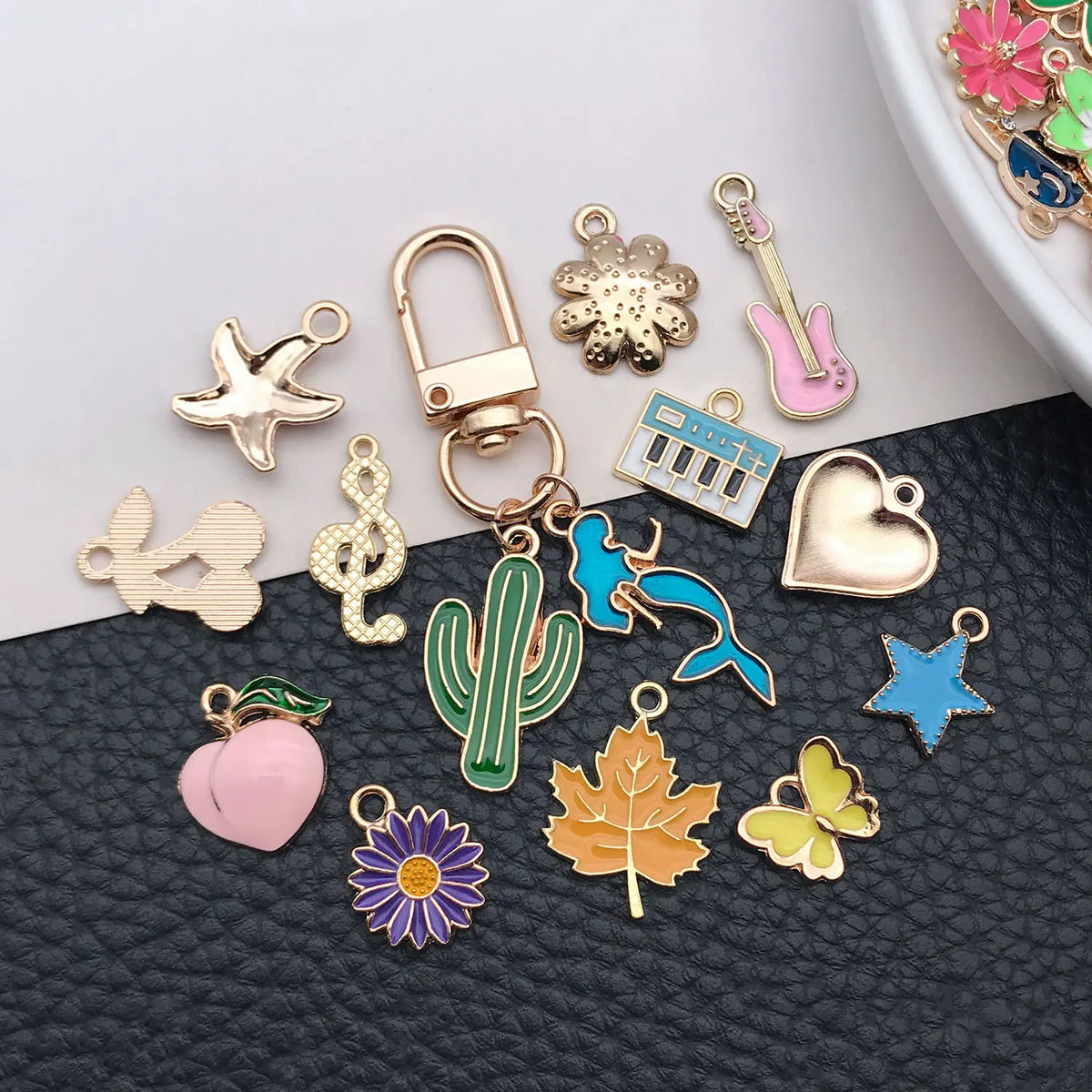 A collection of various enamel alloy flower charms including a star, a cactus, a leaf, and a heart, displayed on a dark surfa