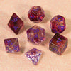 A collection of various colored glitter polyhedral dice including D4, D6, D8, D10, D12, and D20 resting on a pink surface.