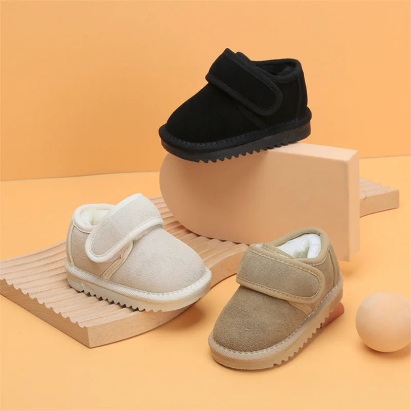 A pair of beige cozy leather winter boots for toddlers with anti-slip rubber soles displayed on a wooden surface.