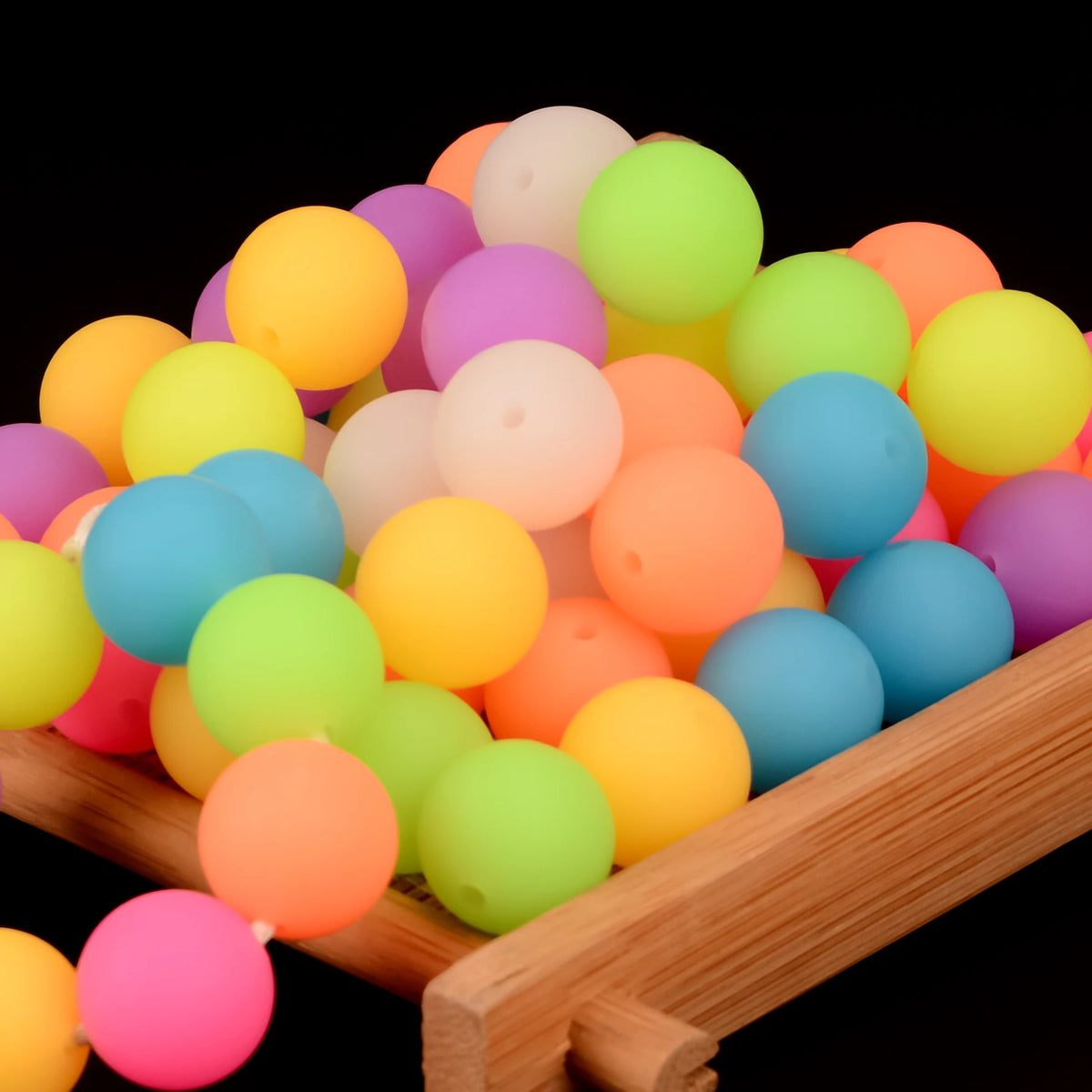 A pile of brightly colored glow-in-the-dark silicone beads in various shades of yellow, green, orange, and pink.