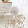 A white plush octopus toy with hanging loops displayed on a gold wire stand.