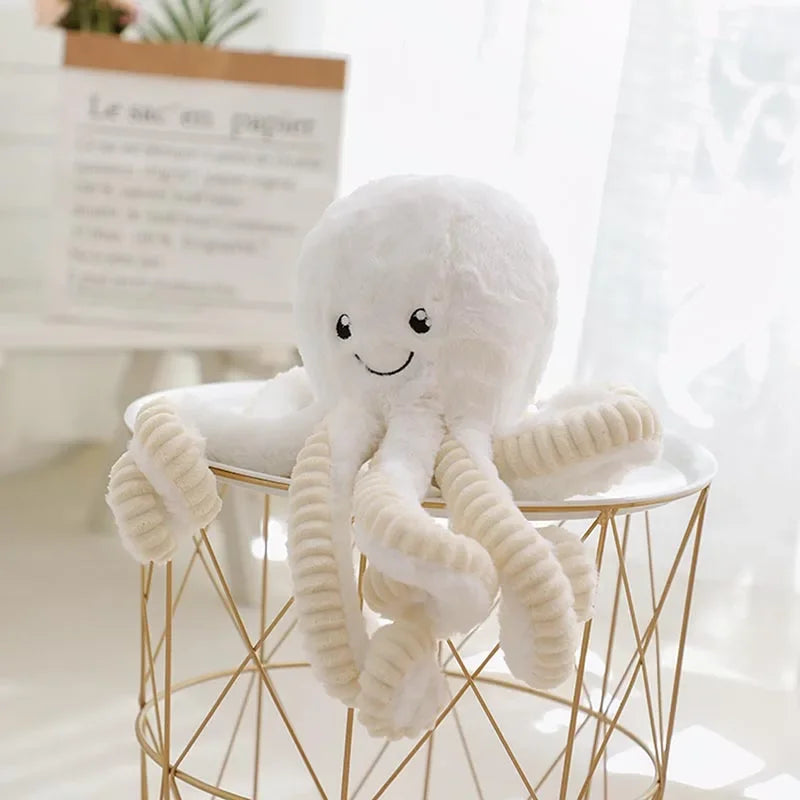 A white plush octopus toy with hanging loops displayed on a gold wire stand.
