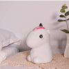 A white unicorn LED night light with a pink horn sits on a woven mat.