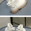 A pair of cream-colored kids winter boots with faux leather detailing and white laces resting on a gray surface.
