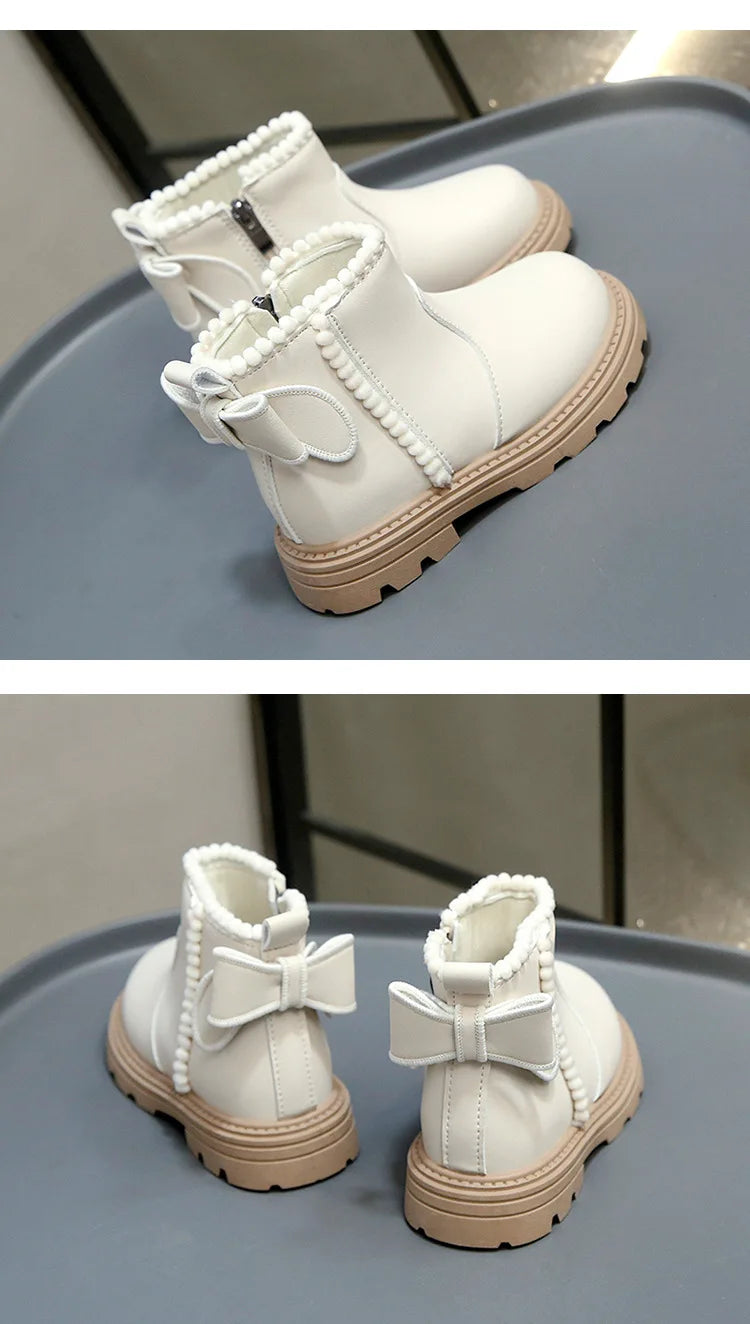 A pair of cream-colored kids winter boots with faux leather detailing and white laces resting on a gray surface.