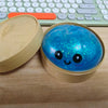 Un jouet anti-stress en forme de dumpling bleu pailleté, avec son contenant ouvert et un clavier.