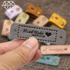 A hand is holding a gray leather-style handmade with love tag among several colorful tags.