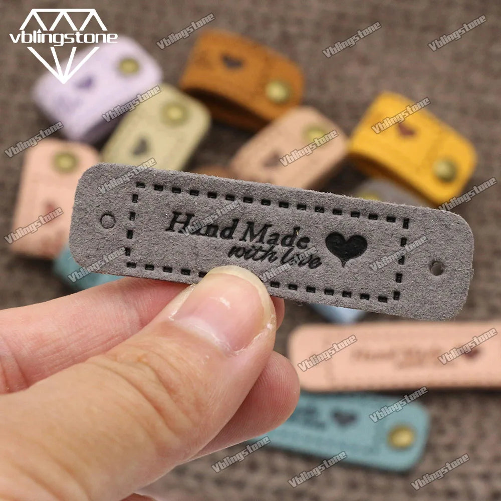 A hand is holding a gray leather-style handmade with love tag among several colorful tags.