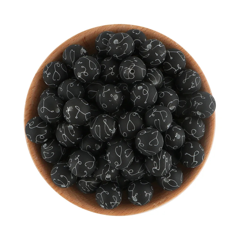 A pile of black printable silicone beads for jewelry making in a wooden bowl.