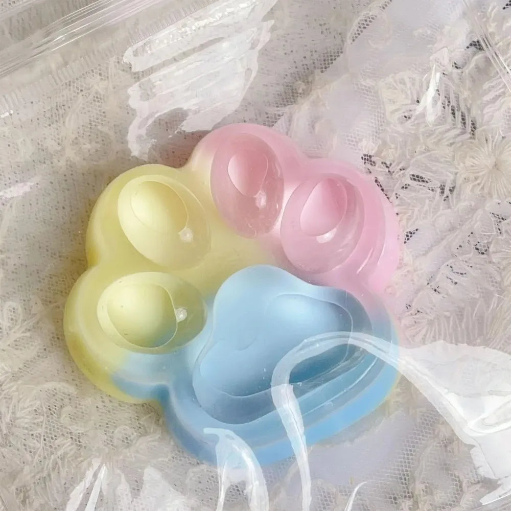 A set of pastel colored squishy toys shaped like cat paws in yellow, pink, and blue.