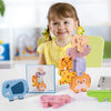 A smiling young girl is holding a stack of wooden animal blocks and shape matching cards on a white table.