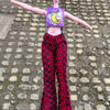 A doll fashion set featuring a purple headpiece with yellow writing and red patterned pants standing on a cobblestone surface