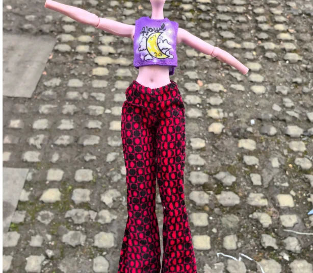 A doll fashion set featuring a purple headpiece with yellow writing and red patterned pants standing on a cobblestone surface