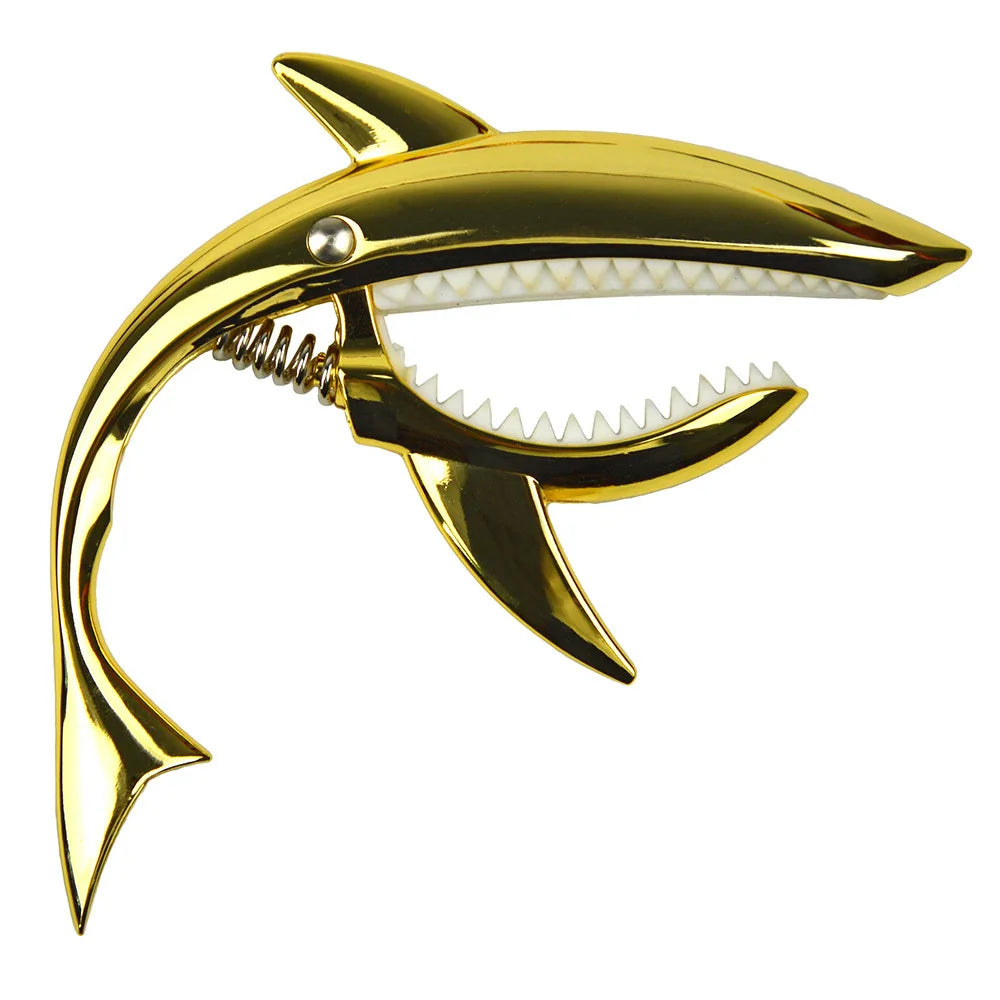 A gold-colored metal shark guitar capo with a serrated edge and a silver tuning peg.