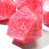A pink resin D20 die with a floral pattern and visible numbers, resting on a white surface.