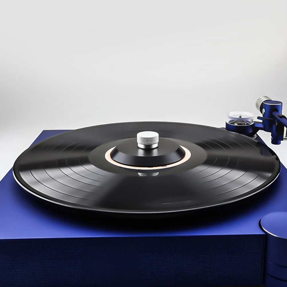 A black aluminum alloy record stabilizer sits on a blue surface next to a turntable.