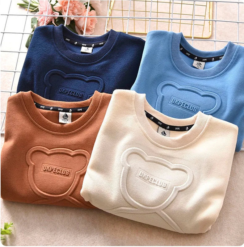 A collection of four kids cartoon bear pullover sweatshirts in navy blue, light blue, terracotta, and cream.
