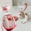 A pink kids pretend play kitchen set featuring a coffee maker, water dispenser, and toaster on a white table.