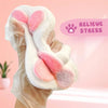 A hand holds a white, fluffy cat paw squishy toy with pink accents, designed to relieve stress.