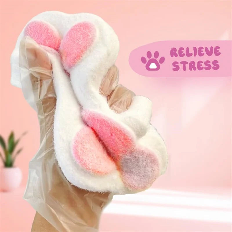 A hand holds a white, fluffy cat paw squishy toy with pink accents, designed to relieve stress.