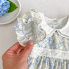 A close-up of a light blue floral dress for girls showing the ruffled neckline and white lace trim.