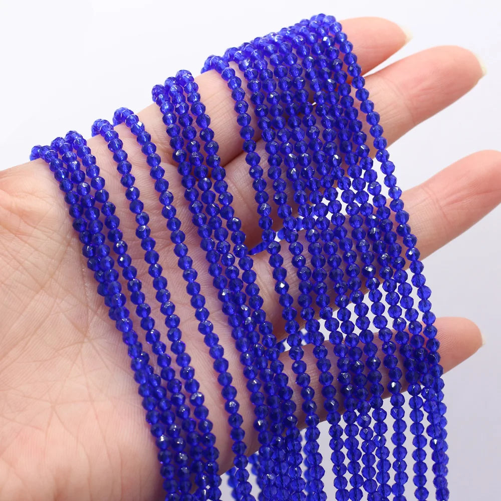 A hand holds multiple strands of small, faceted natural blue beads for DIY jewelry making.