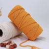A spool of natural orange cotton macrame rope with loose strands lying nearby.