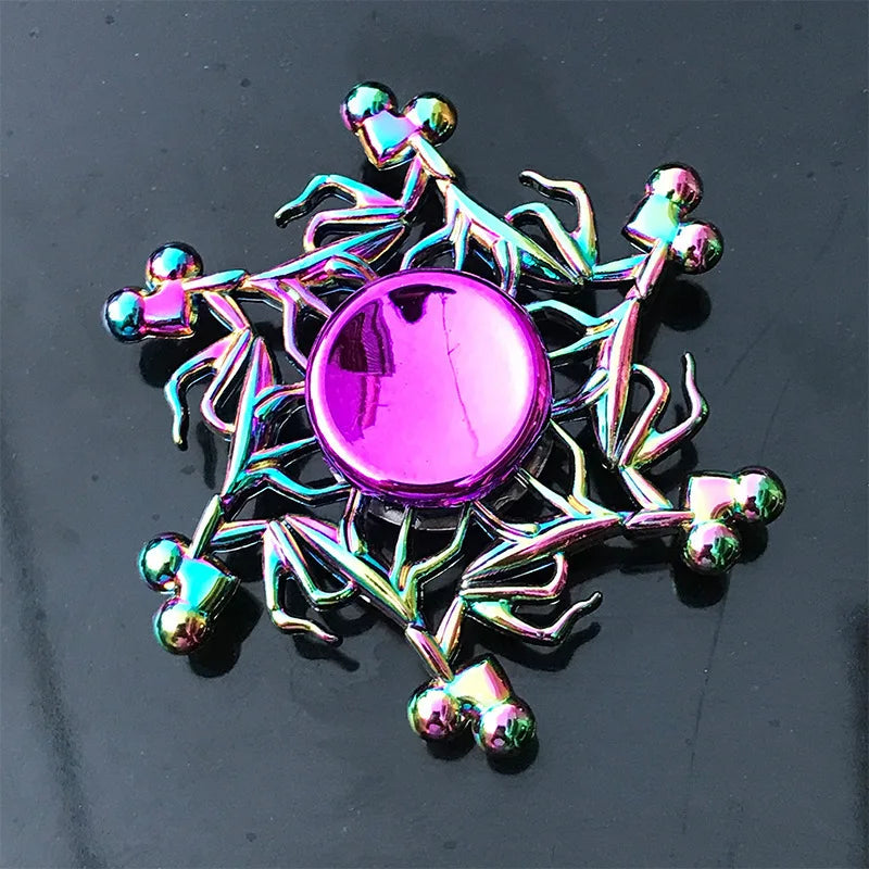 A colorful metal fidget spinner with a pink center and silver wire arms, resting on a dark surface.