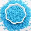 A pile of bright blue polymer clay slice sprinkles in a white dish on a white background.