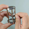 A hand holds a multi-layer stainless steel puzzle cage brain teaser with intersecting bars.