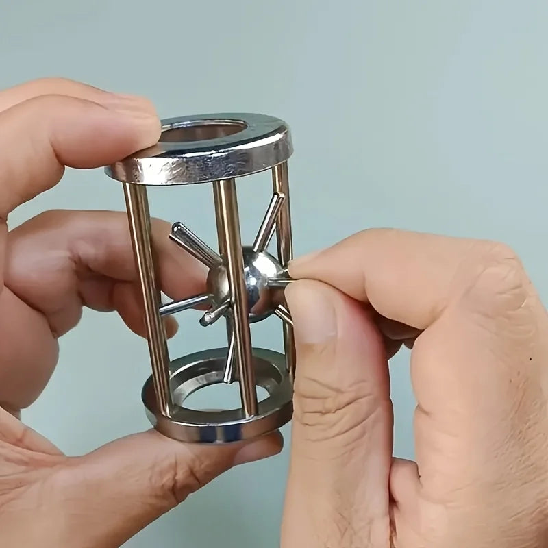 A hand holds a multi-layer stainless steel puzzle cage brain teaser with intersecting bars.