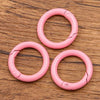 A set of ten pink metal O-ring spring clasps arranged on a wooden surface.