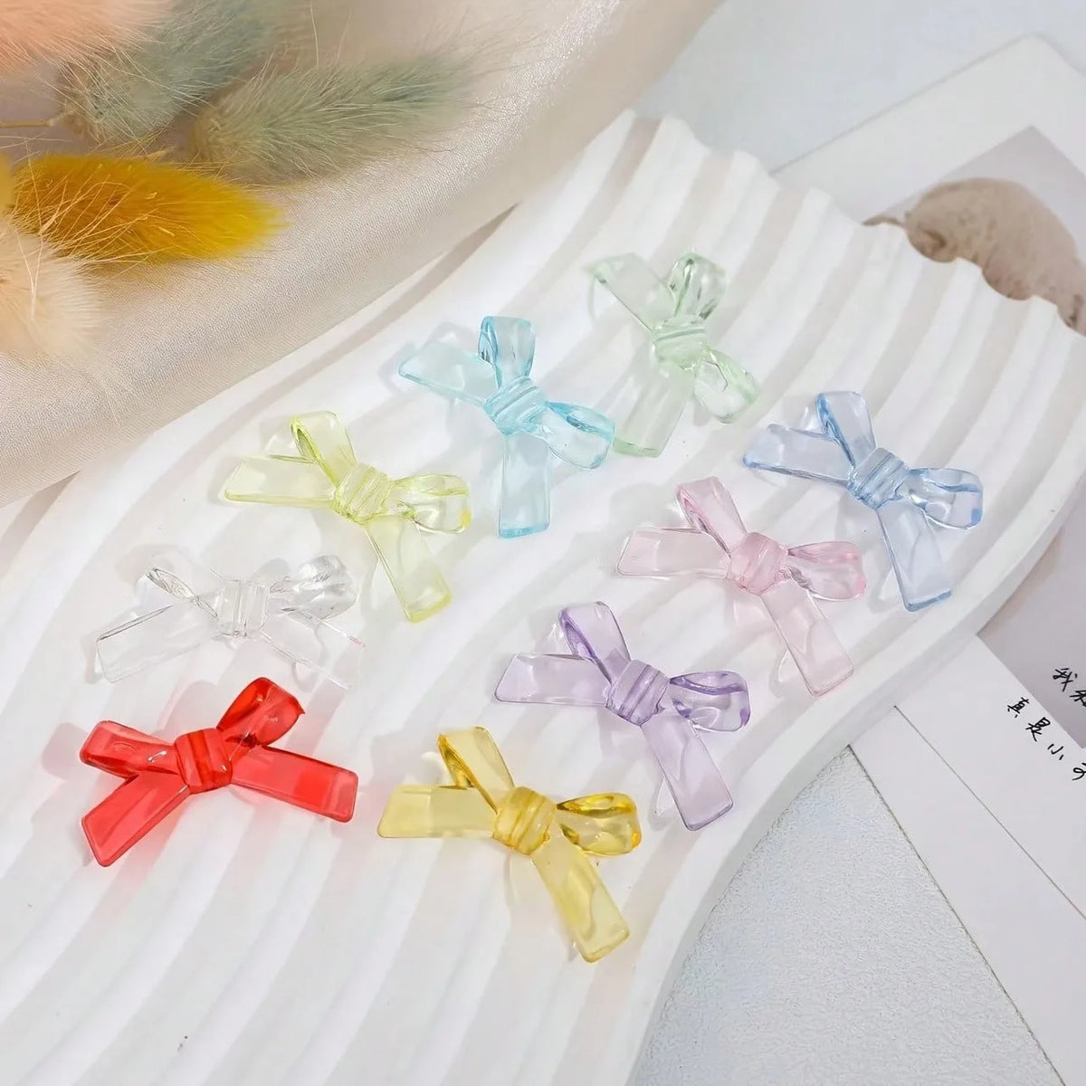 A collection of clear and pastel acrylic bow tie beads in various shades are displayed on a white surface.