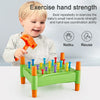 A toddler is playing with a green toy that features orange and yellow nails for hand strength exercise.