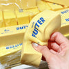 A hand holds a yellow putty shaped like a putter, next to packaged butter fidget toys.