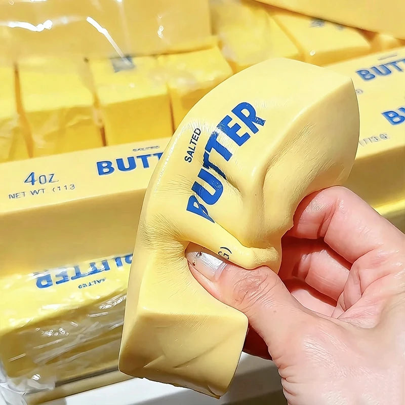 A hand holds a yellow putty shaped like a putter, next to packaged butter fidget toys.