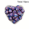 A collection of ten purple and blue floral printed silicone beads in a white dish.