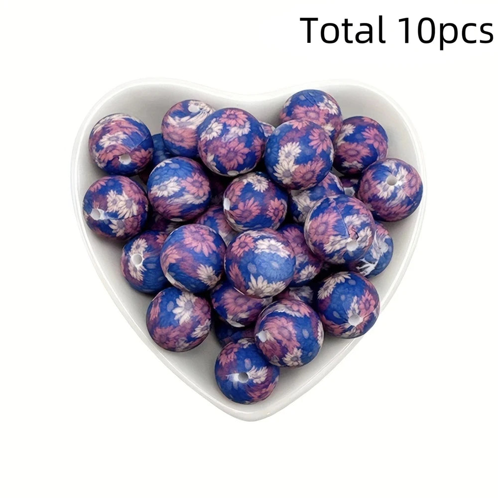 A collection of ten purple and blue floral printed silicone beads in a white dish.