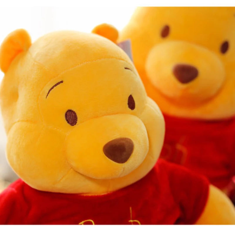 A yellow plush toy resembling Winnie the Pooh character with a brown nose and red clothing.
