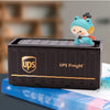 A small, light blue, cartoon-like figurine is placed on top of a black UPS Freight storage box.