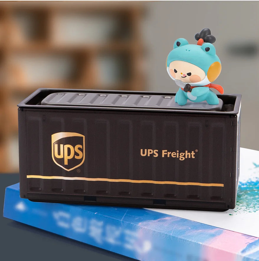 A small, light blue, cartoon-like figurine is placed on top of a black UPS Freight storage box.
