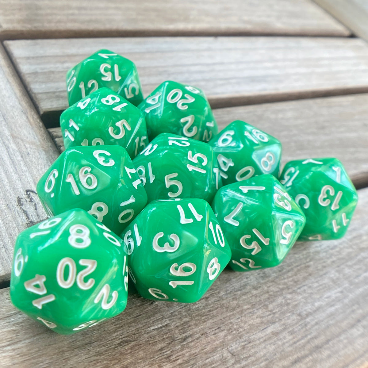 A collection of ten green pearl acrylic D20 dice scattered on a wooden surface.