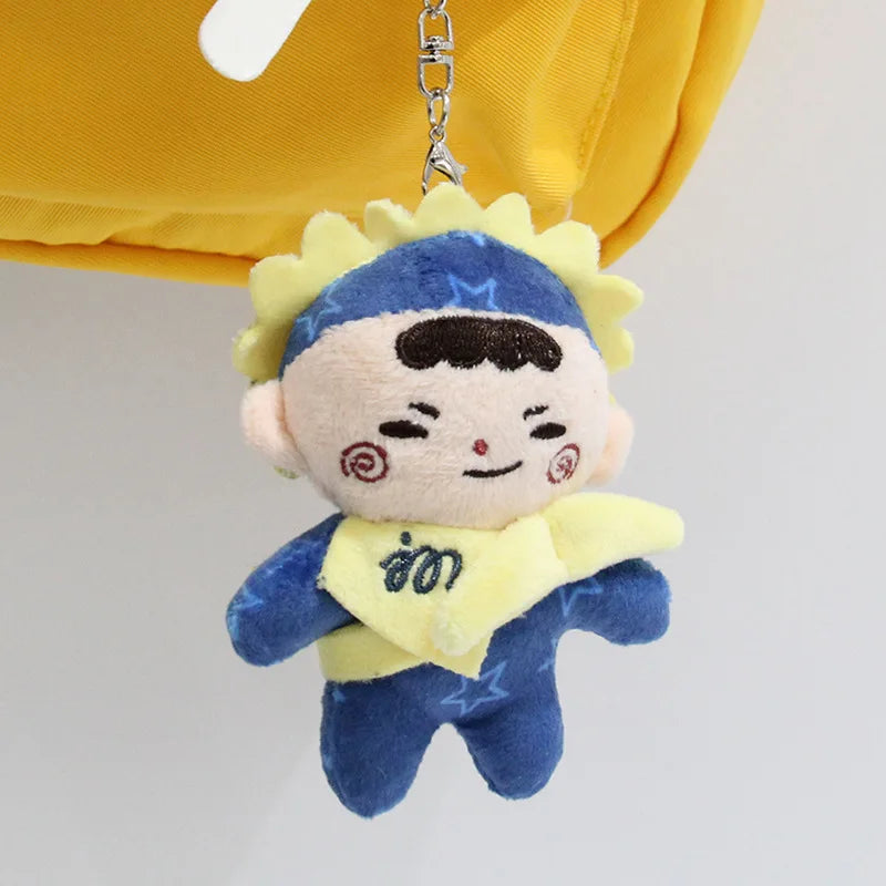 A plush pendant doll of a male character with blue skin and yellow hair against a yellow fabric background.
