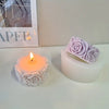 A white silicone rose candle mold with a pink rose is displayed next to a lit candle.